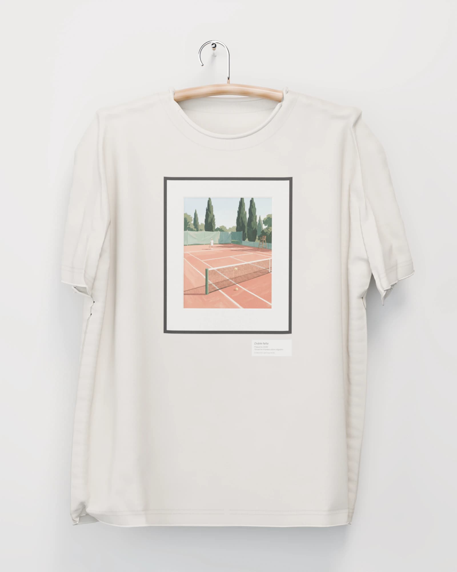 Polera color hueso colgada de una percha de madera en un muro claro, con una cancha de arcilla con un tenista lejos y una pelota atrapada en la red, en marco negro con paspartú en el pecho