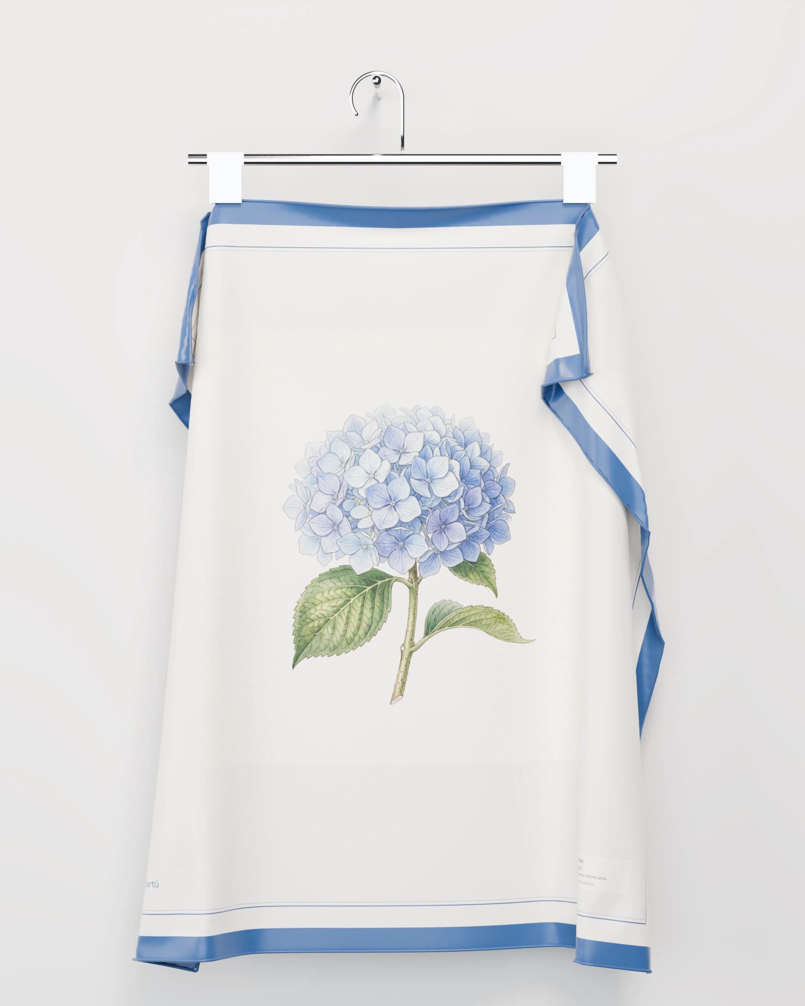 Pañuelo de seda cuadrado colgado de una percha cromada con dos pinzas: una hortensia azul pintada como lámina botánica, un borde azul y la cartela en la esquina