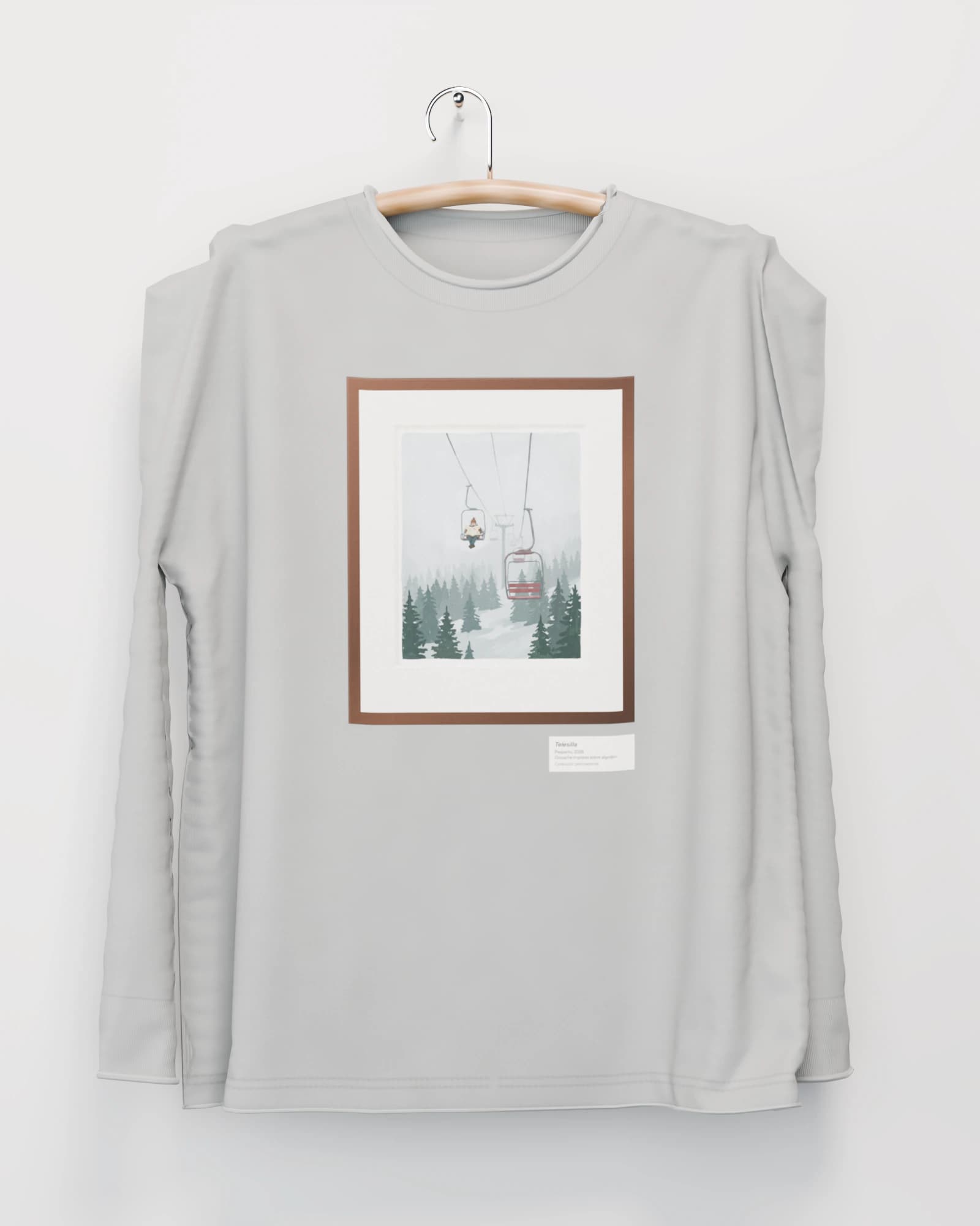 Polera manga larga color gris niebla colgada de una percha de madera en un muro claro, con un telesilla que sube en la niebla con una silla roja vacía, en marco de nogal en el pecho
